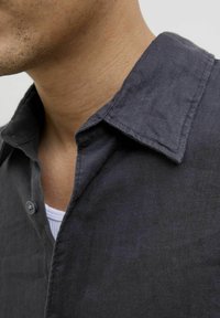 Camisa de lino gris oscuro con cuello, cierre de botones, textura visible y una camiseta blanca parcialmente visible debajo del cuello.