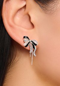 Schwarze und silberne bogenförmige Ohrringe mit Kettenakzenten, verziert mit klaren Strasssteinen für zusätzliche Details; an einem Ohr präsentiert.