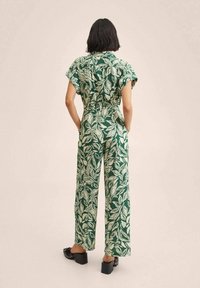 Mono verde con estampado de hojas, mangas cortas, corte holgado y piernas anchas. Tejido texturizado y costuras visibles. Zapatos negros de tacón grueso.