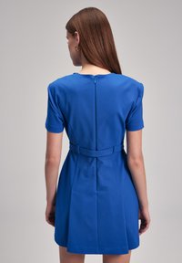 Blue short-sleeve dress featuring a fitted waist, zipper closure at the back, and two front pockets. Smooth texture and structured shape.