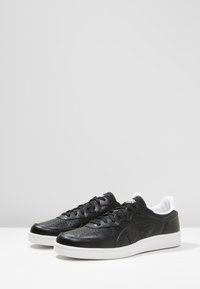 Sneaker in pelle nera con design perforato, suola in gomma bianca e rivestimento interno bianco a contrasto. Presenta una chiusura tradizionale con lacci.