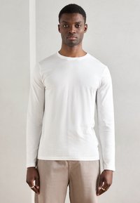 Balta ilga rankovė marškinėliai iš švelnios, lygaus medvilnės su apvaliu iškirpimu, derinami su šviesiai bežinėmis kelnėmis. Paprastas ir minimalistiškas dizainas.