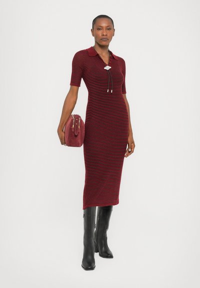 Knit dress in burgundy with horizontal black stripes, featuring a polo collar, short sleeves, and a side slit, paired with a red handbag and black boots.