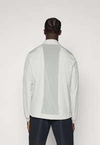 Lightweight jacket in pale gray with a sheer mesh panel at the back, long sleeves, and a collar, featuring a straight-cut hem.