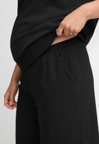 Zwarte broek van een gestructureerde stof, met een elastische tailleband en zijzak, gecombineerd met een eenvoudig zwart top.