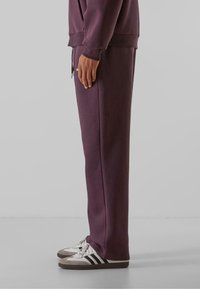 Lilla sweatpants lavet af blødt stof, med et afslappet fit, sidelommer og elastisk talje. Sættes sammen med hvide sneakers.