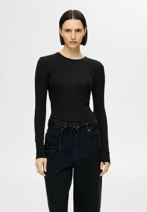 Svart ribbad långärmad topp med rund halsringning, kombinerad med högmidjade mörka jeans med dragsko i midjan och avslappnad passform.