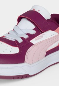 Παιδικό αθλητικό παπούτσι Puma σε λευκό, ροζ και σκούρο ροζ με αυτοκόλλητο ιμάντα και κορδόνια, με το λογότυπο της μάρκας στο πλάι και στη γλώσσα.