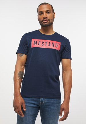 Marineblaue Baumwoll-T-Shirt mit kurzen Ärmeln und einem rechteckigen roten Logo mit der Aufschrift "MUSTANG" auf der Brust. Weiche Textur.