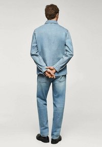 Giacca in denim blu chiaro e jeans a vestibilità rilassata. L'outfit presenta un colletto classico e una texture uniforme. Scarpe nere completano il look.