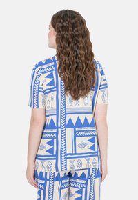 Maglietta in cotone con un motivo geometrico blu e beige, maniche corte e vestibilità rilassata, decorata con disegni di pesci e foglie.
