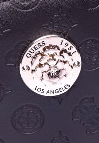 Borsa a tracolla in pelle nera con motivo stampato, hardware in tonalità argento e chiusura floreale con l'incisione "GUESS 1981 LOS ANGELES".