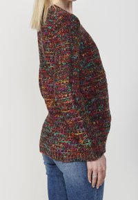 Meerkleurige gebreide trui met een gestructureerd patroon. Ronde halslijn, lange mouwen en een licht getailleerde pasvorm. Gecombineerd met blauwe jeans.