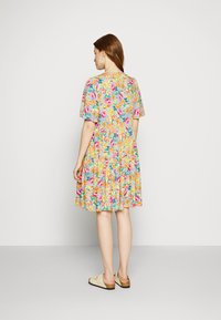 Vestido curto de mangas curtas com fundo azul claro, apresentando padrões em rosa, amarelo e verde; até os joelhos com uma barra rodada.