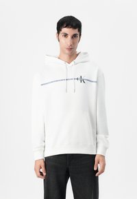 Witte hoodie met een trekkoord, een voorzak en het CK-logo op de linkerborst. Heeft een marineblauwe streep en een zachte, gestructureerde stof.