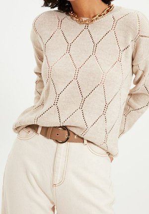 Beige strikket sweater med diamantmønster i hulstrik kombineret med lyse højttaljede bukser og et brunt bælte med rund spænde.