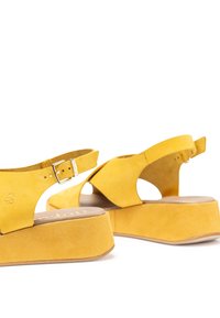 Gelbe Wildleder-Plateausandalen mit verstellbarem Schnallenverschluss, offener Zehenpartie und ausgeschnittenem Seitendesign auf einem dicken Absatz für zusätzliche Stabilität.