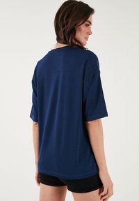 Námořnická modrá oversized tričko vyrobené z měkké látky, s kratšími rukávy a kulatým výstřihem, s hladkým, jednoduchým vzhledem.