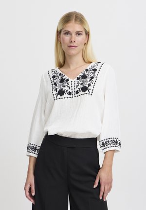 White blouse with black floral embroidery on the neckline and sleeves, featuring a V-neck design and lightweight, textured fabric.