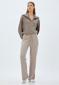 Conjunto de ropa de estar en color beige con textura acanalada, que incluye una parte superior con cuello de cremallera y mangas anchas, y pantalones a juego con cintura ajustable y dobladillos acampanados.