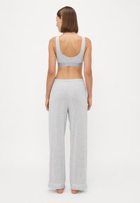 Sivi bralette s širokim izrezom na leđima, u kombinaciji s labavim sivim lounge hlačama s manžetama na rubovima i ravnim pojasom. Glatka tekstura kroz cijeli materijal.
