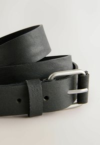 Black leather belt coiled with a silver rectangular metal buckle on a light neutral background.