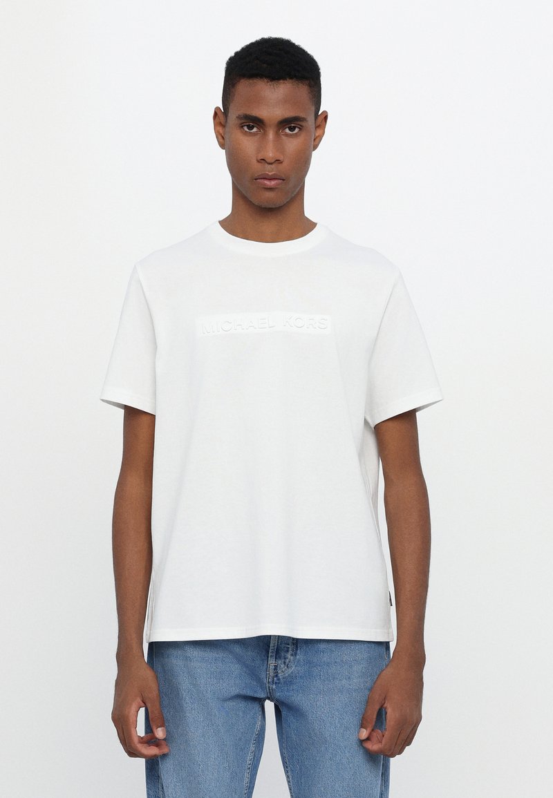 White cotton T-shirt featuring a textured, embossed Michael Kors logo on the front, round neck, and short sleeves.