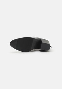Schwarze Schuhsohle mit einer glatten, abgerundeten Zehe und einer strukturierten, gerippten Oberfläche für besseren Halt. Verstärkter Absatz mit rutschfester Gestaltung.
