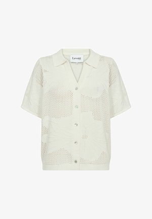 Fehér, rövid ujjú kötött kardigán, melynek gallérja és gombos záródása van. Az anyag texturált, nyitott kötésű mintával rendelkezik.