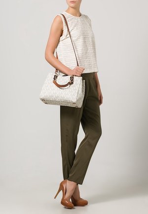 Bolso blanco con patrón y asa marrón, combinado con una blusa beige texturizada y pantalones verde oliva. Zapatos de tacón marrones completan el conjunto.