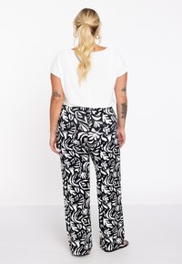 Haut blanc à manches courtes associé à un pantalon large à motifs de feuilles noir et blanc, avec une texture lisse et une coupe ample pour le confort.