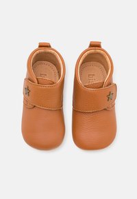 Zapatos para niños pequeños de cuero color marrón claro con punta redondeada, cierre de correa y un acento en forma de estrella, con una textura suave. Diseño ligero.