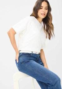 Wit T-shirt met korte mouwen en een losse pasvorm, gecombineerd met blauwe denim jeans met een slanke snit en een witte riem. De textuur lijkt glad.