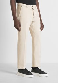 Pantalones de algodón beige con un diseño de pierna recta, que cuentan con herrajes negros, costuras detalladas y bolsillos laterales. Combinados con zapatillas negras.