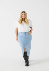 Svetlomodrá rifľová sukňa s predným rozparkom, skombinovaná s bielym tričkom. Modelka má na sebe čierne čižmy po kolená. Hladká textúra a priliehavý strih.