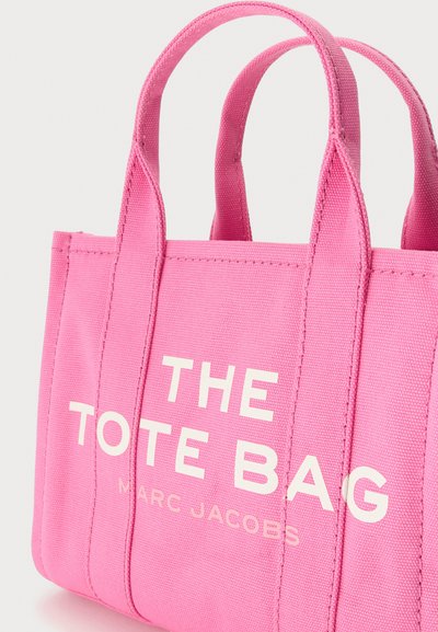 Petit sac cabas en toile rose vif avec deux anses et texte blanc en gras « THE TOTE BAG » ainsi qu’un texte plus petit « MARC JACOBS » à l’avant.