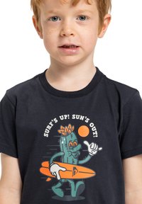 Námořnické tričko s grafikou kaktusu, který drží oranžovou surfovací desku, s textem "SURF'S UP! SUN'S OUT!" v bílé a oranžové barvě.