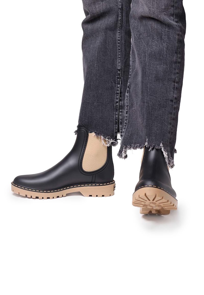 Bottes Chelsea en cuir noir avec côtés élastiques beige et semelles épaisses beige, portées avec un jean gris foncé à ourlet effiloché.