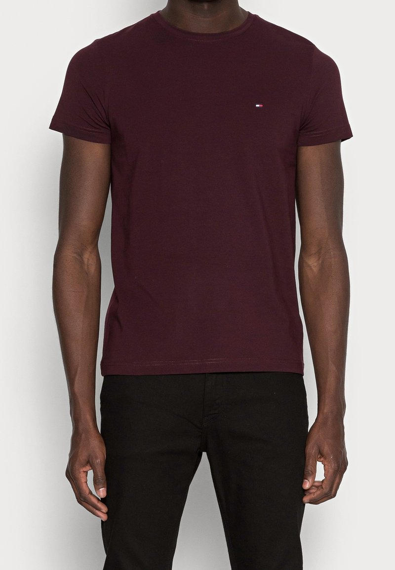 Bordeaux bomuld t-shirt med korte ærmer, rund halsudskæring og et lille broderet logo på brystet. Bæres sammen med sorte bukser.