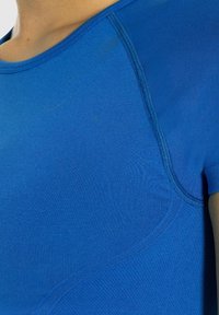Maglietta sportiva blu con una vestibilità aderente, texture liscia e dettagli delle cuciture a contrasto. Il tessuto sembra leggero e traspirante.