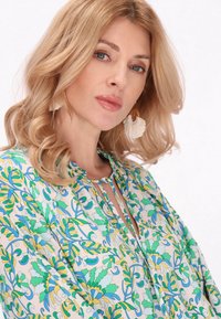 Blusa a maniche lunghe in tessuto leggero con motivo floreale nei colori verde, blu e giallo, con colletto arricciato e apertura a chiave.