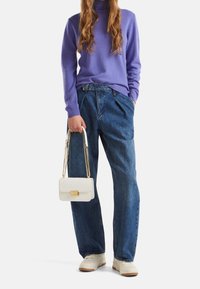 Jasnofioletowy sweter z golfem, luźne niebieskie dżinsy, biała torebka ze złotymi elementami, białe trampki, swobodny, casualowy strój.