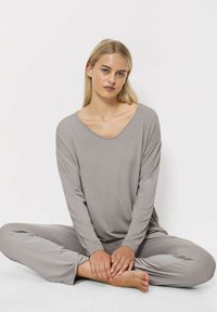 Jasnoszary komplet odzieży domowej składający się z luźnej bluzki z długim rękawem i spodni, wykonany z miękkiego materiału. Znaczący dekolt w serek i swobodny krój.