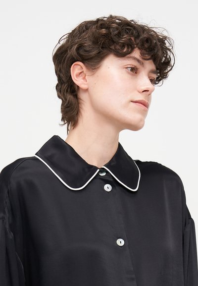 Black satin shirt featuring a large rounded collar with white trim and buttons, characterized by a loose fit and smooth texture.