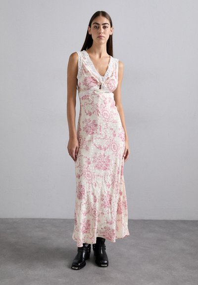 Maxi dress in cream with pink floral patterns, featuring a v-neck, lace trim, and gathered waist. Paired with black ankle boots.