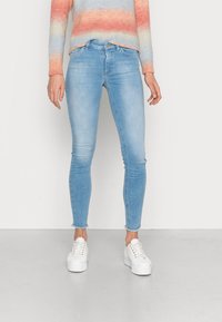 Vaaleansiniset slim fit -farkut, joissa on istuva muotoilu, lievää kulumista helmassa, yhdistetty valkoisiin tennareihin.