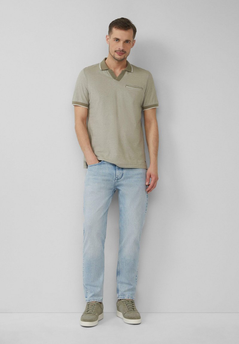 Oliwkowa koszulka polo z dekoltem w serek, kontrastowymi wykończeniami i kieszonką na piersi. Zestawiona z jasnoniebieskimi dżinsami i szarymi sneakersami.