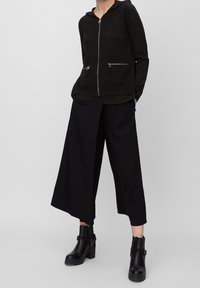 Black zipped hoodie with a hood and two zippered pockets, paired with wide-leg black trousers. Includes ankle boots with a chunky heel.
