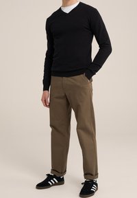 Svart V-ringad tröja, beige byxor och svarta sneakers med vita ränder. Materialet verkar mjukt; tröjan passar tätt runt kroppen.