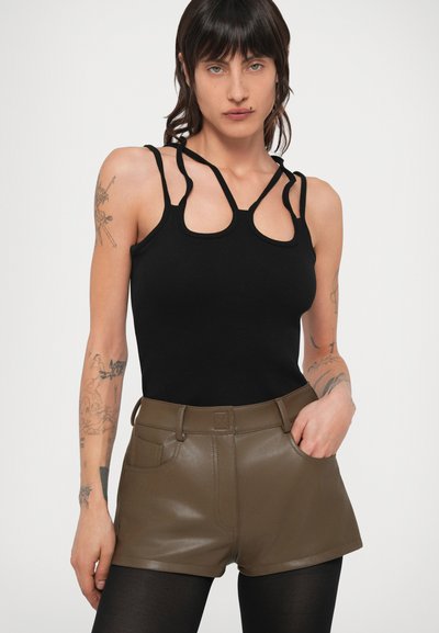 Top preto canelado com alças recortadas únicas, combinado com calções de cintura alta e brilhantes em verde-oliva, com bolsos frontais.